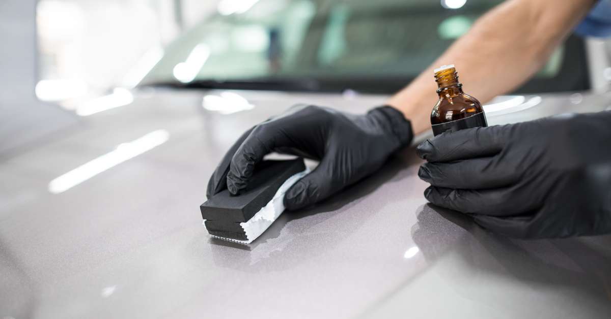 A professional auto detailer wearing rubber gloves holds a bottle of liquid for cleaning the vehicle’s surface.